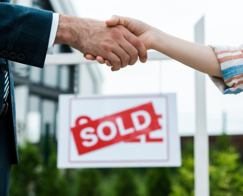 selective focus of broker and woman shaking hands near board with sold letters